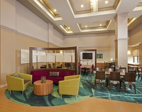 Bright lobby seating area with colorful chairs, round table, and dining tables under coffered ceiling at Marriott SpringHill Suites Naperville/Warrenville.