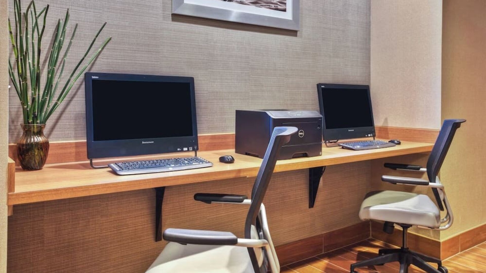 Business center with two desktop computers, keyboard and mouse setups, wood desk, and office chairs against textured wall at Marriott SpringHill Suites Naperville/Warrenville.