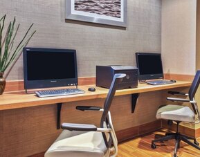 Business center with two desktop computers, keyboard and mouse setups, wood desk, and office chairs against textured wall at Marriott SpringHill Suites Naperville/Warrenville.