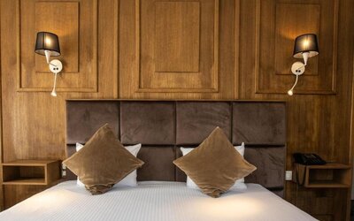 Double bed with padded headboard, wood-paneled wall, and wall-mounted lamps creating a warm, cozy setting at Hôtel Espérance.
