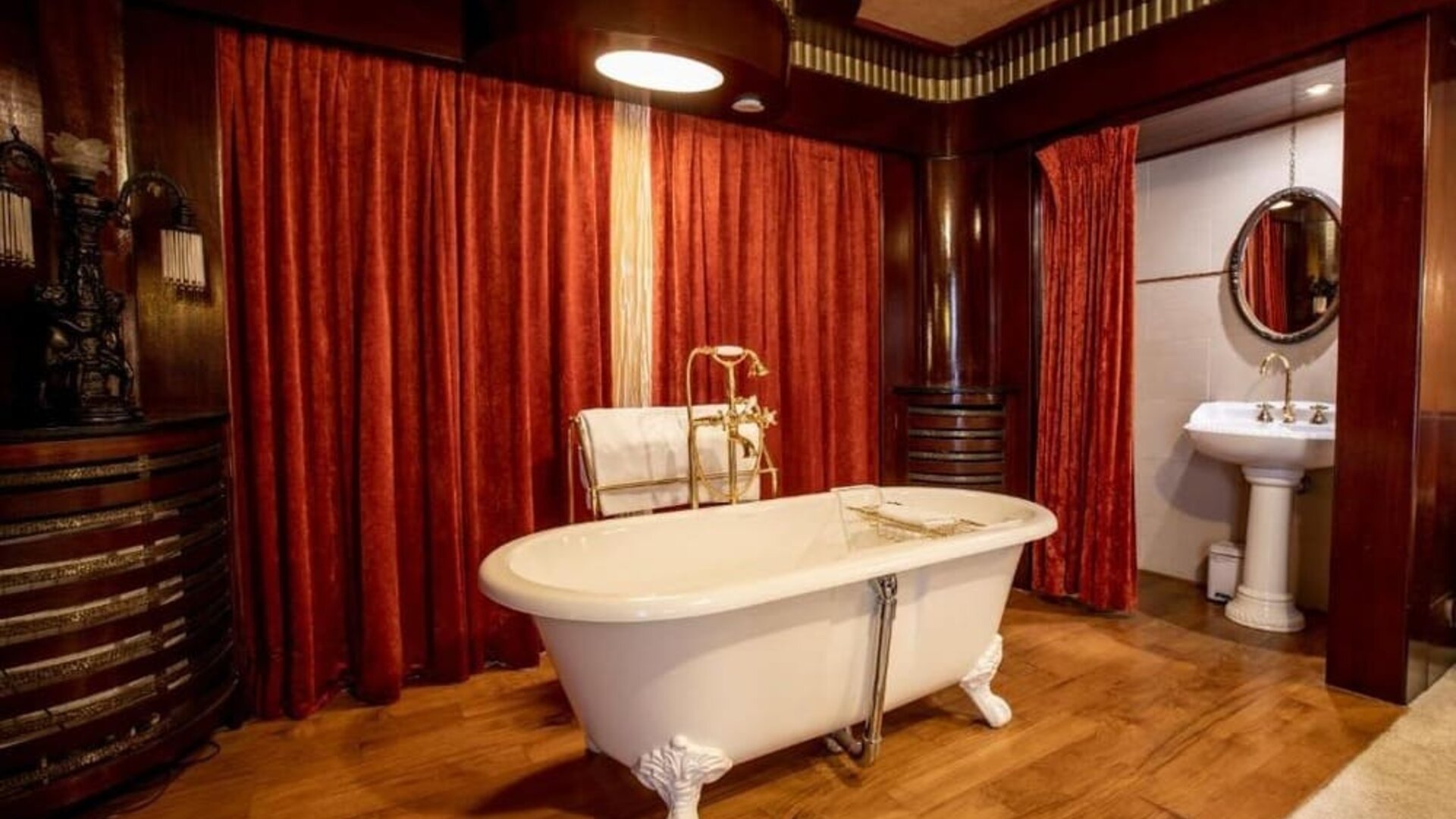 Freestanding clawfoot bathtub with brass fixtures set against red drapes and wood-paneled walls at Hôtel Espérance.