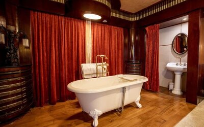 Freestanding clawfoot bathtub with brass fixtures set against red drapes and wood-paneled walls at Hôtel Espérance.
