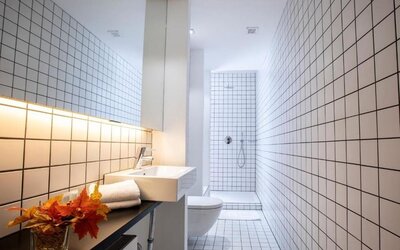 Modern tiled bathroom with wall-mounted sink, toilet, walk-in shower, and minimalist lighting at Hôtel Espérance.