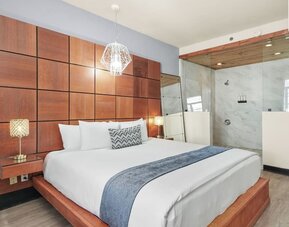 King bedroom with wood-paneled headboard wall, glass-partition shower, and modern lighting at Chesterfield Hotel & Suites.
