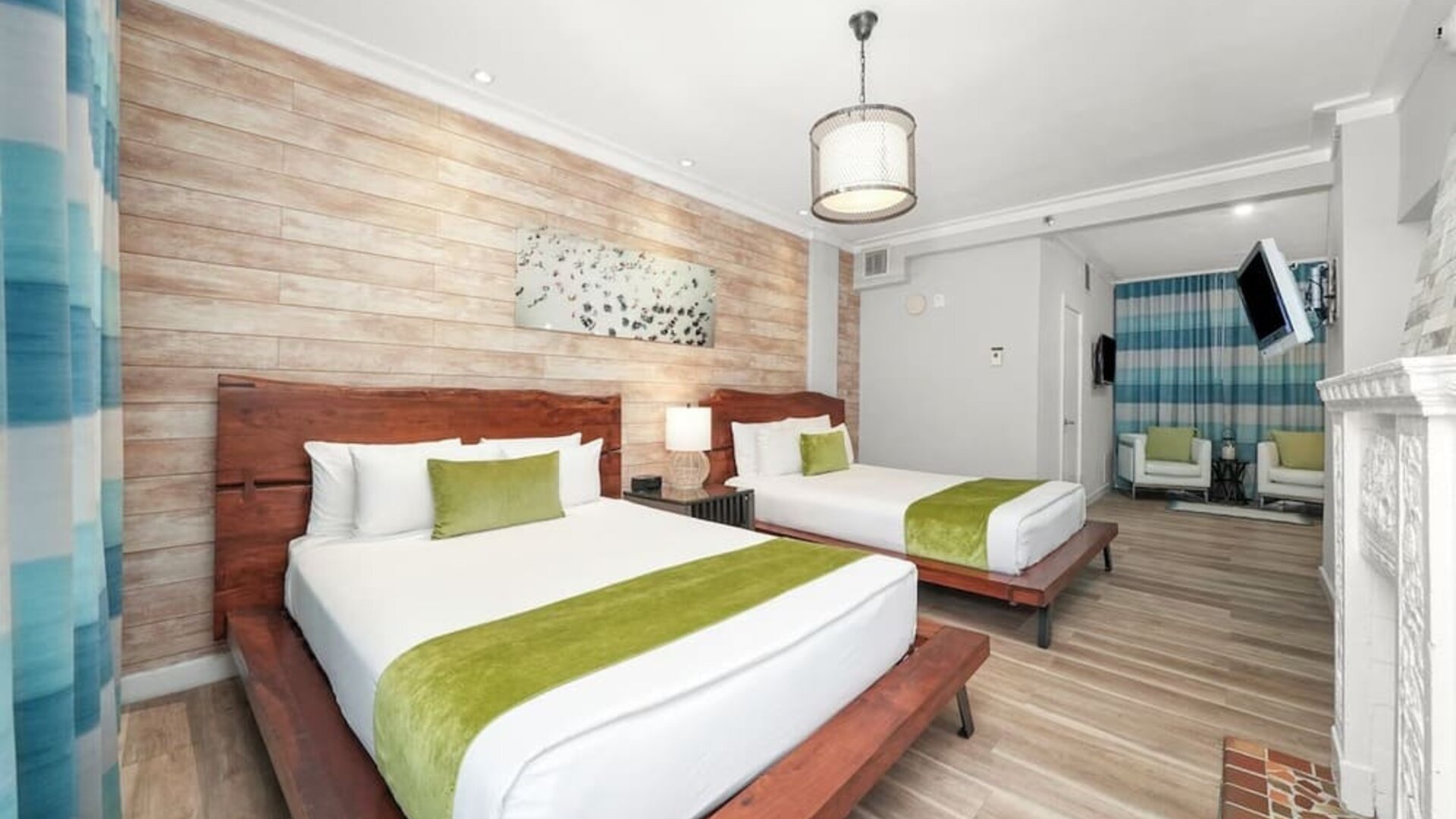 Guest room with two beds, wood headboards, green runners, seating area, and wall-mounted TV at Chesterfield Hotel & Suites.