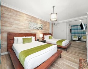 Guest room with two beds, wood headboards, green runners, seating area, and wall-mounted TV at Chesterfield Hotel & Suites.