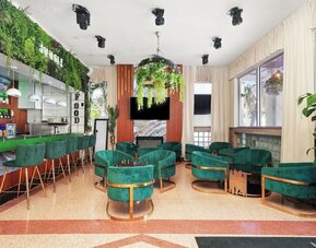 Modern lounge bar with green seating, pendant lights, marble feature wall, and indoor plants at Chesterfield Hotel & Suites.