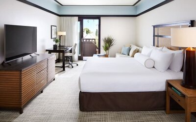 Bright guest room with king bed, desk, TV console, and balcony access with outdoor seating at The Ambrose Hotel Santa Monica.