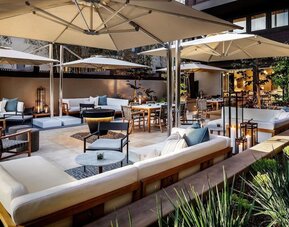 Cozy courtyard patio with cushioned seating, dining tables, umbrellas, and ambient evening lighting at The Ambrose Hotel Santa Monica.