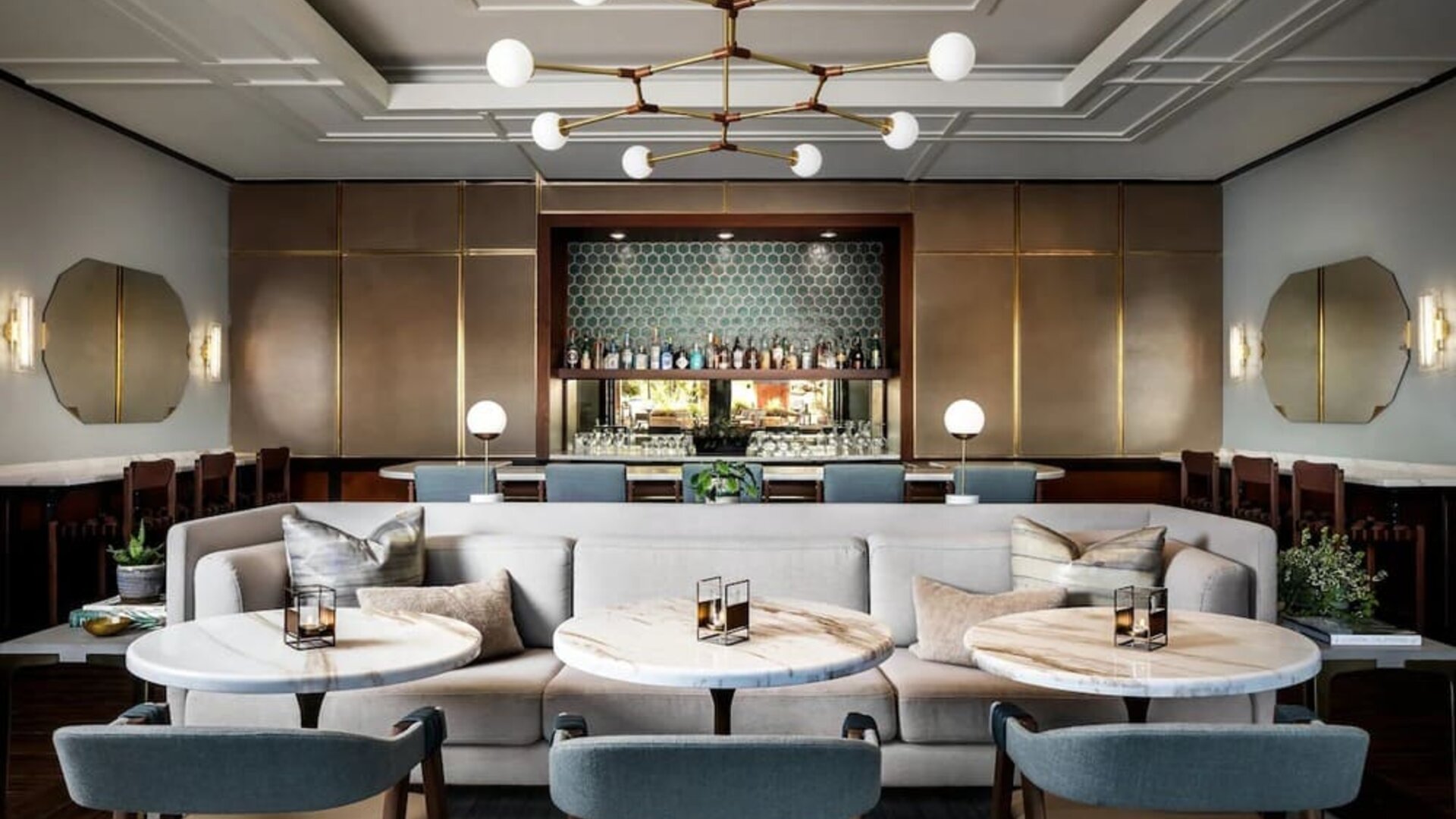 Stylish lounge dining space with cushioned seating, round tables, and backlit bar display at The Ambrose Hotel Santa Monica.