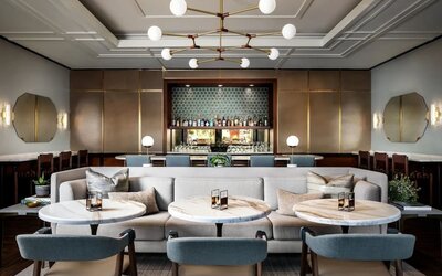 Stylish lounge dining space with cushioned seating, round tables, and backlit bar display at The Ambrose Hotel Santa Monica.