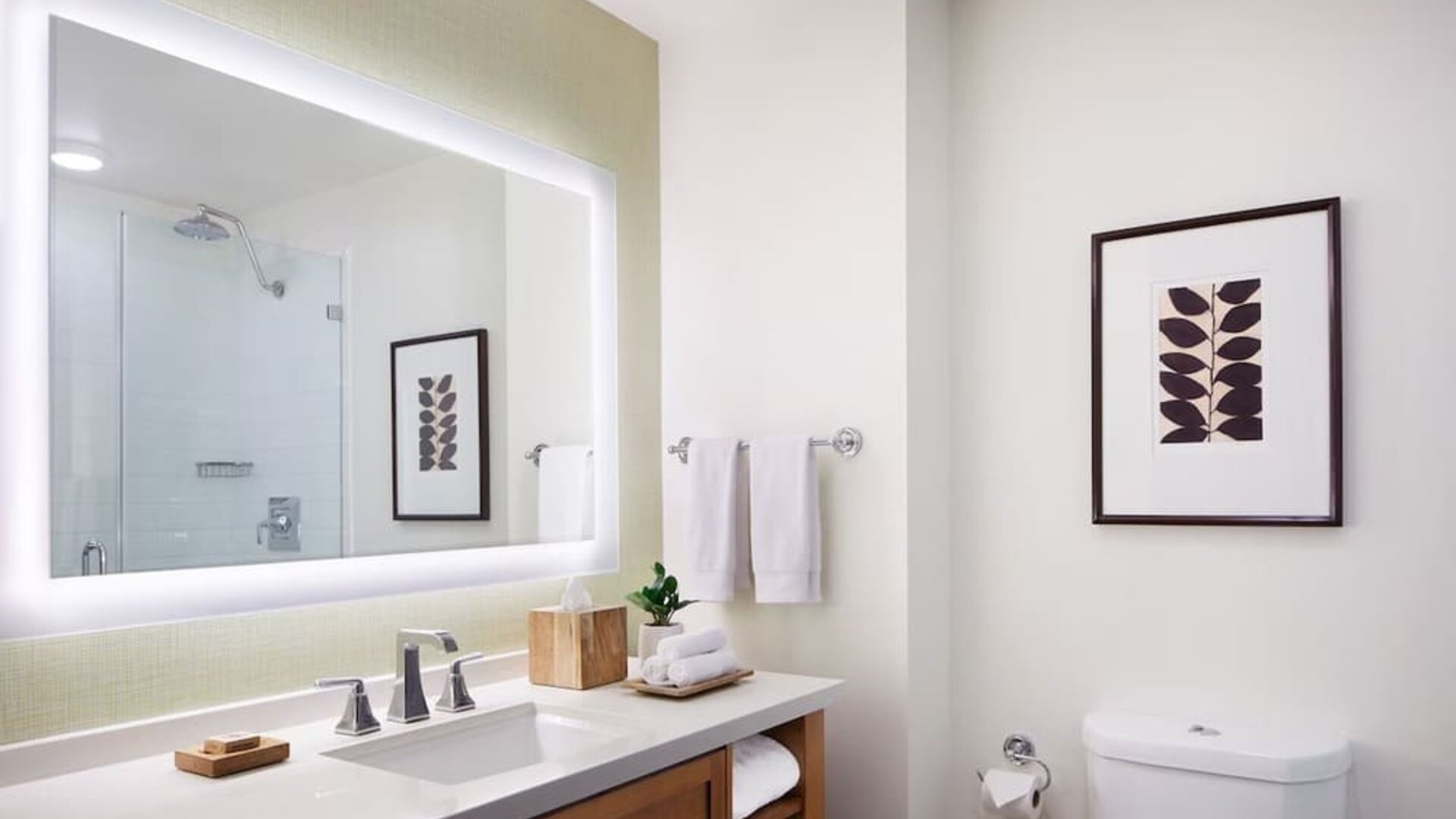 Modern bathroom with large illuminated mirror, vanity, and clean white finishes at The Ambrose Hotel Santa Monica.