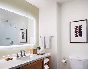 Modern bathroom with large illuminated mirror, vanity, and clean white finishes at The Ambrose Hotel Santa Monica.