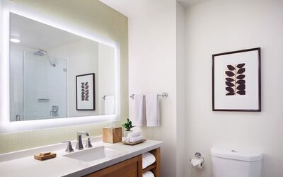 Modern bathroom with large illuminated mirror, vanity, and clean white finishes at The Ambrose Hotel Santa Monica.