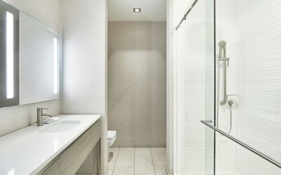 Modern bathroom with long vanity, illuminated mirror, glass shower enclosure, and neutral tile finishes at AC Hotel By Marriott Beverly Hills.