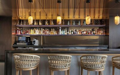 Sleek bar with backlit shelves, bottle display, pendant lighting, and woven bar stools at AC Hotel By Marriott Beverly Hills.