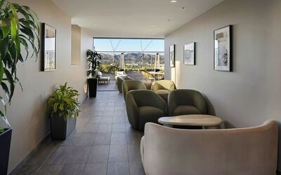 Lounge corridor with cushioned seating, small tables, plants, and open view toward outdoor terrace at AC Hotel By Marriott Beverly Hills.