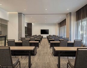 Meeting room with rows of tables and chairs, presentation screen, and large windows with curtains at AC Hotel By Marriott Beverly Hills.