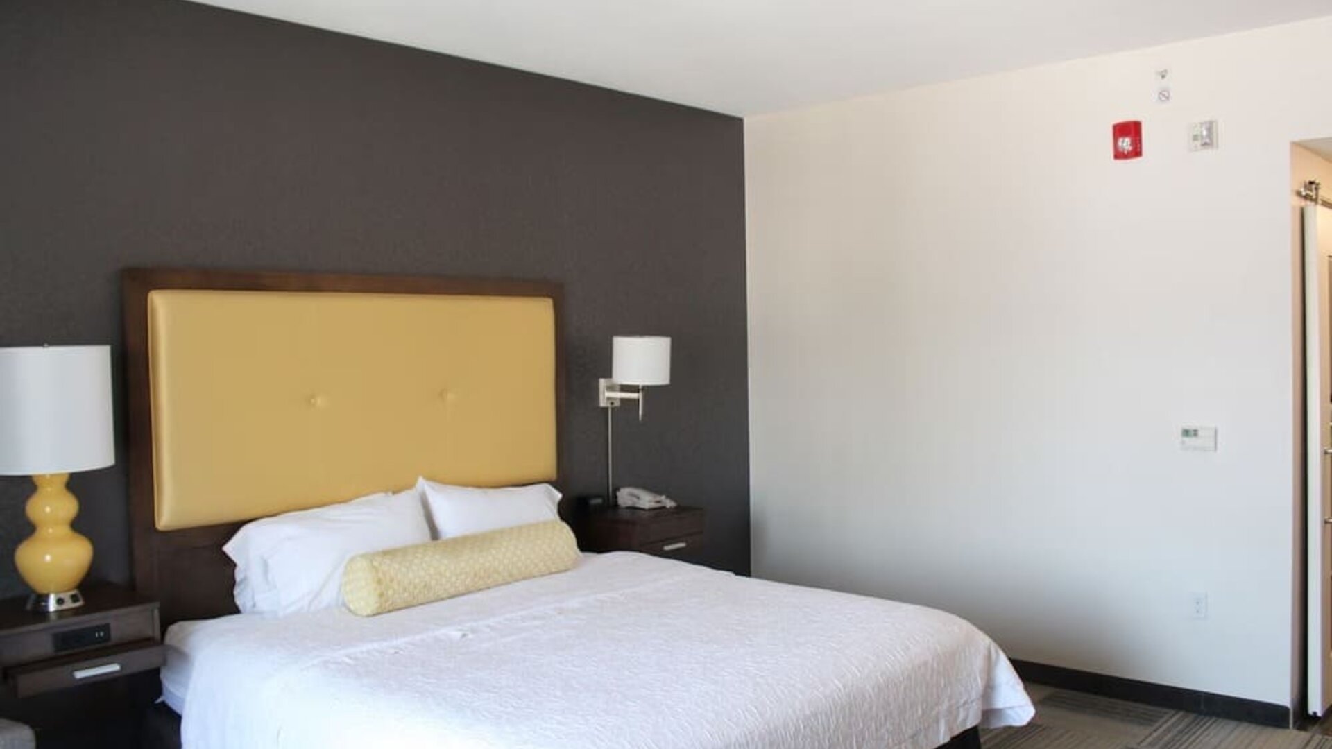 Bright guest room with king bed, accent wall, bedside lighting, and minimalist layout at Hampton Inn & Suites Los Angeles / Hollywood.