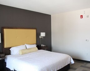 Bright guest room with king bed, accent wall, bedside lighting, and minimalist layout at Hampton Inn & Suites Los Angeles / Hollywood.