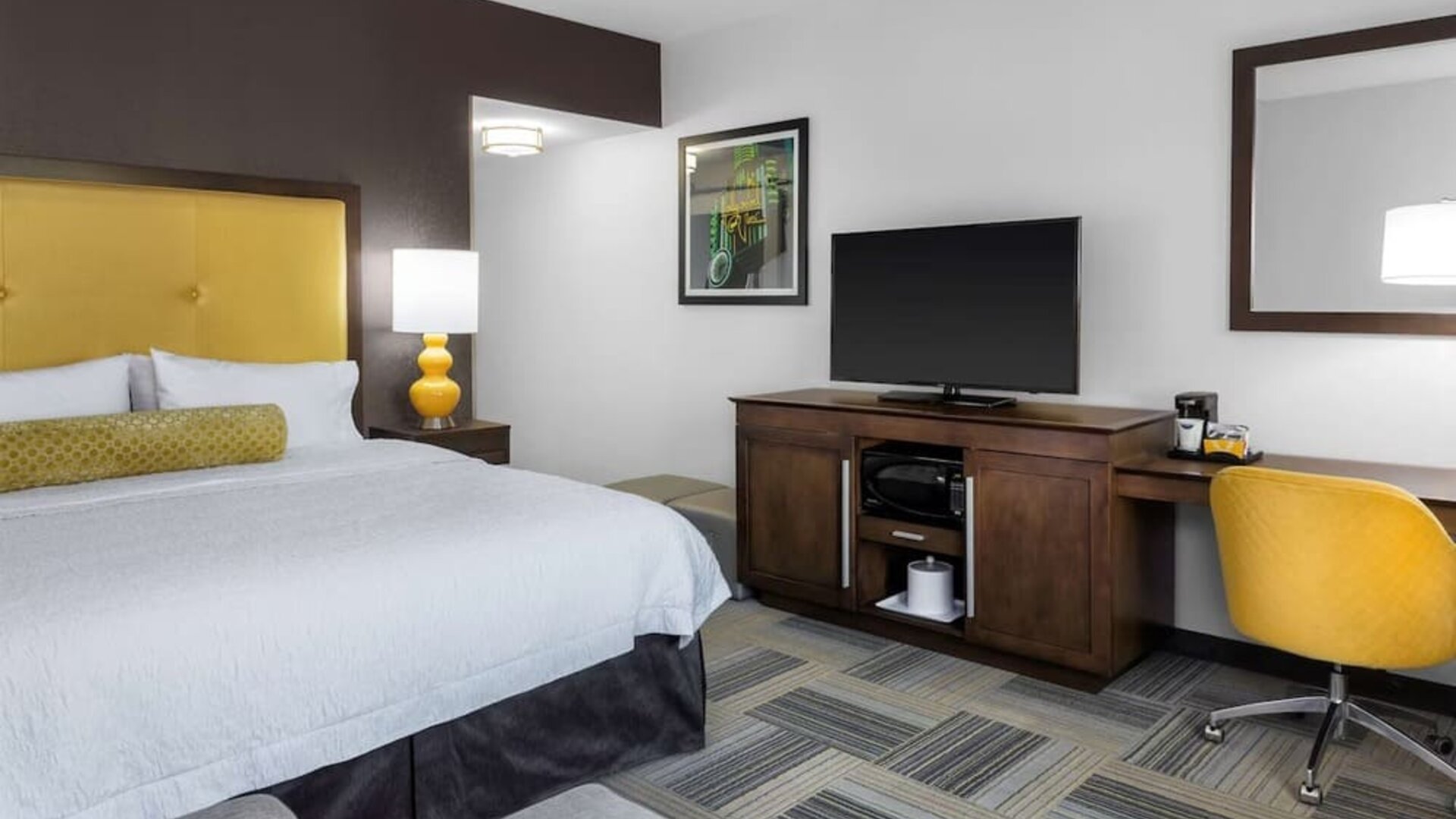 Guest room with king bed, yellow upholstered headboard, work desk, TV, and modern furnishings at Hampton Inn & Suites Los Angeles / Hollywood.
