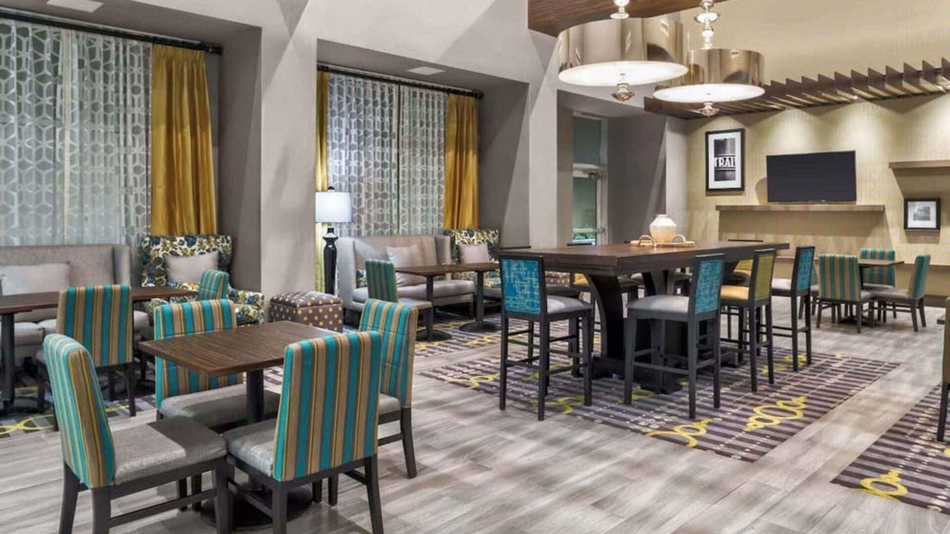 Dining/lounge area with patterned chairs, communal tables, warm lighting, and contemporary décor at Hampton Inn & Suites Los Angeles / Hollywood.
