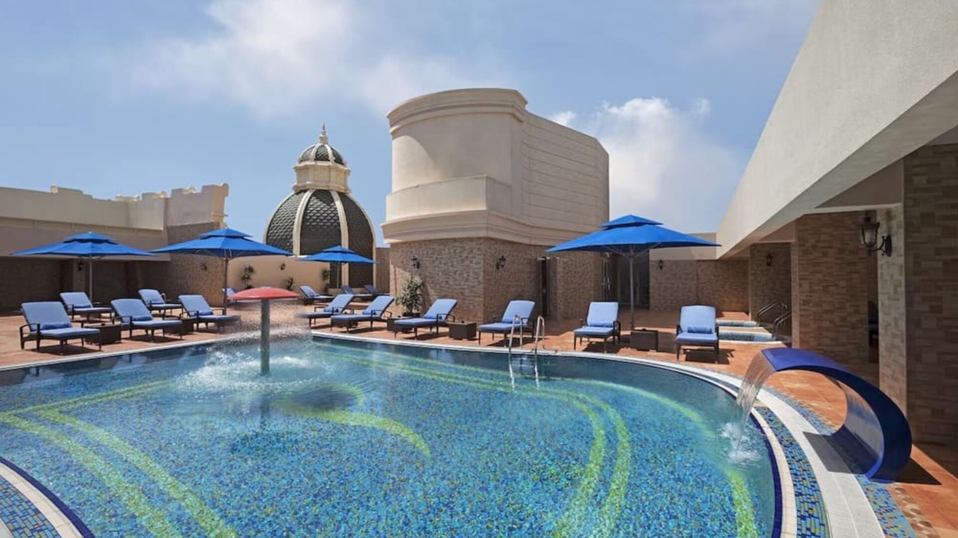 Outdoor pool with blue loungers, umbrellas, water features, and surrounding terrace seating