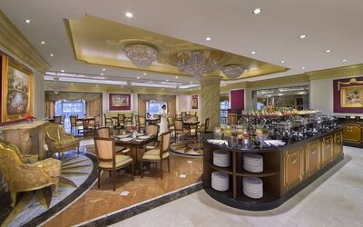 Spacious dining room with buffet station, chandeliers, and multiple tables arranged across marble floors