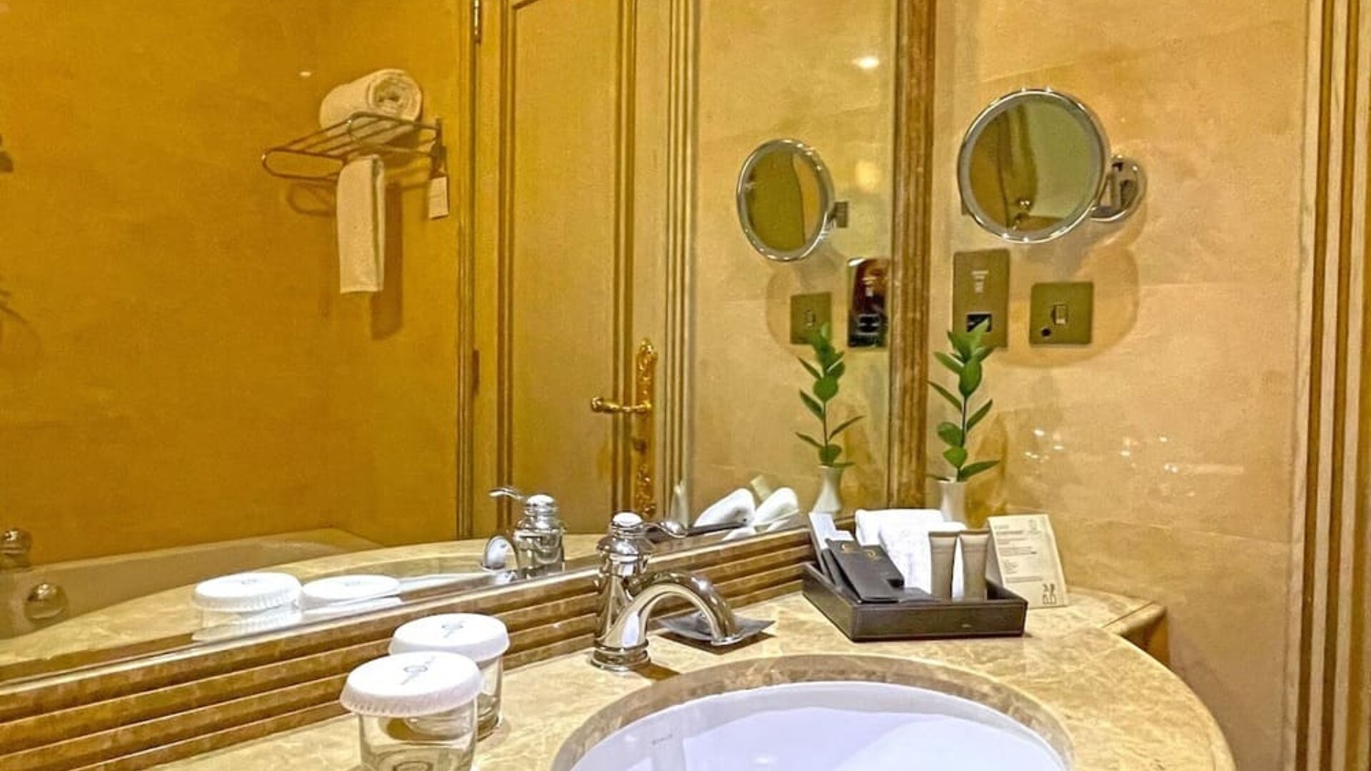 Marble bathroom vanity with round sink, large mirror, toiletries tray, and warm gold-toned finishes