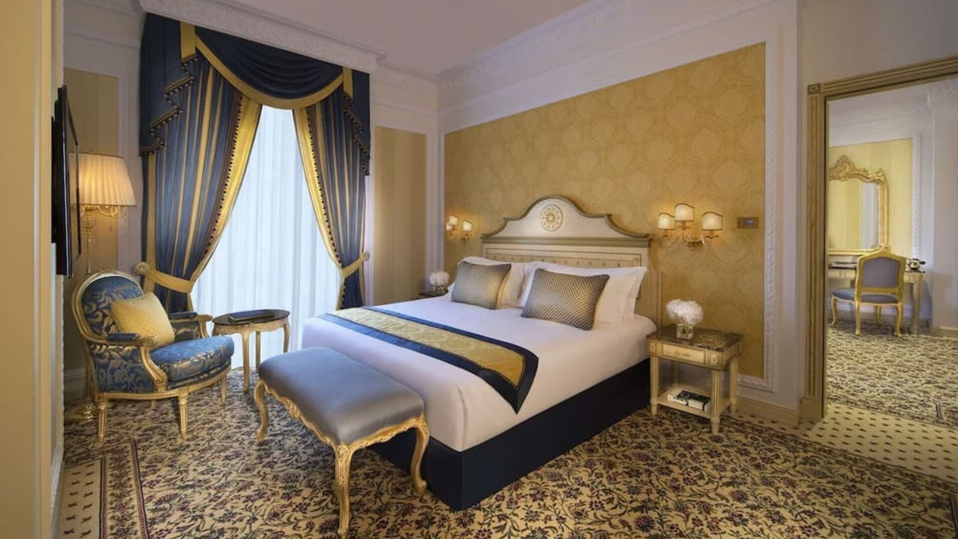 Classic bedroom with blue drapes, upholstered bench, and ornate furniture beside a large bed