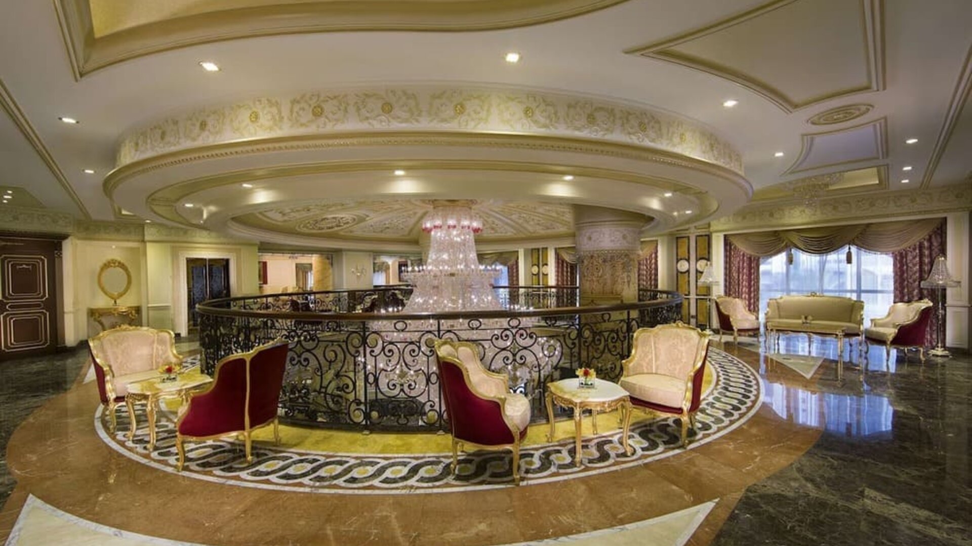 Upper-level lounge with curved railing, chandelier, and clusters of upholstered chairs and tables