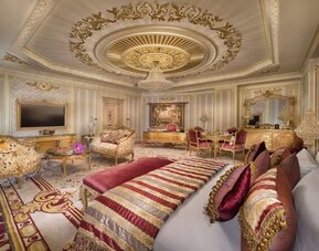 Luxurious suite with red and gold decor, ornate furniture, chandelier, and large bed
