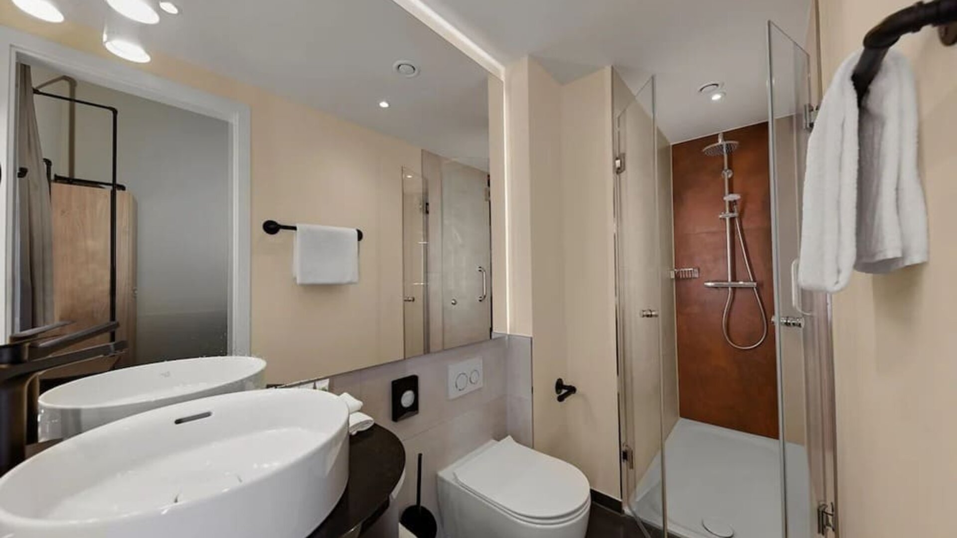 Modern bathroom with double sinks, large mirror, walk-in shower, and wall-mounted toilet