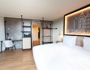 King bed with white linens, wall art headboard, and narrow windowed corridor leading to separate seating area