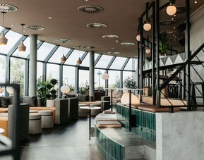 Restaurant space with floor-to-ceiling windows, bar counter, hanging lights, and casual seating areas