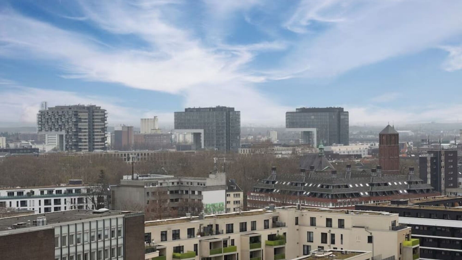 Elevated city view with modern buildings, rooftops, and cloudy sky stretching across the skyline