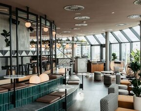 Open dining area with modern seating, greenery, bar section, and slanted glass ceiling allowing daylight