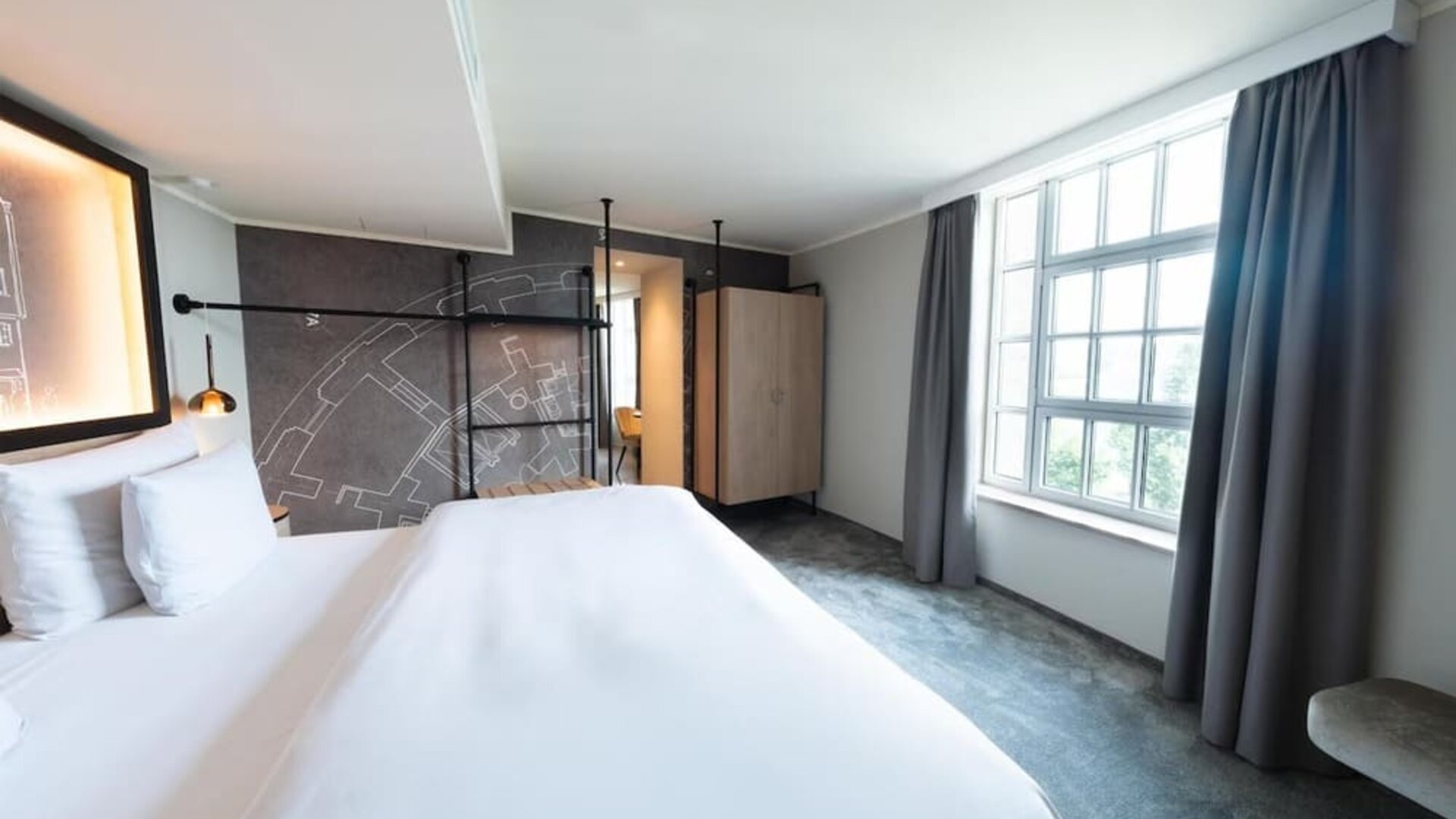 Minimalist bedroom with king bed, gray accent wall, wardrobe, and large window with curtains drawn aside