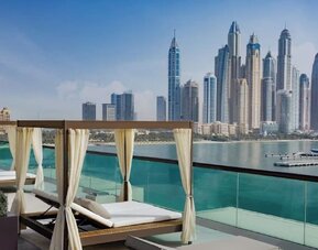 Private cabanas with cushioned loungers on terrace overlooking calm water and modern skyline