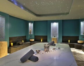 Spa treatment room with massage table, candles, mosaic tile walls, and soft ambient lighting