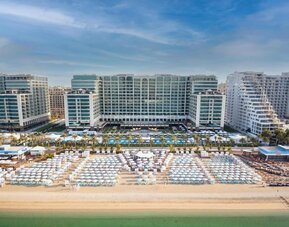 Beachfront hotel exterior with large pool, rows of loungers, and multi-story buildings facing the sea