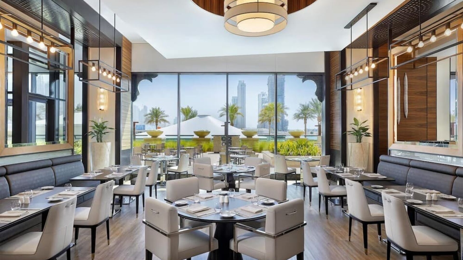 Restaurant dining room with upholstered chairs, pendant lights, and floor-to-ceiling windows to terrace