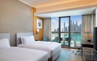 Twin bed guest room with balcony, seating area, and clear view of water and skyline through glass doors