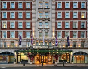 Red brick hotel exterior with lit entrance canopy, flags, and symmetrical rows of windows along the facade