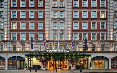 Red brick hotel exterior with lit entrance canopy, flags, and symmetrical rows of windows along the facade