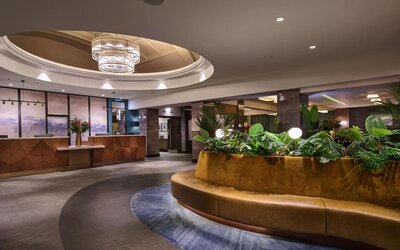 Hotel lobby with circular seating around indoor planter, chandelier above, and reception desk in background