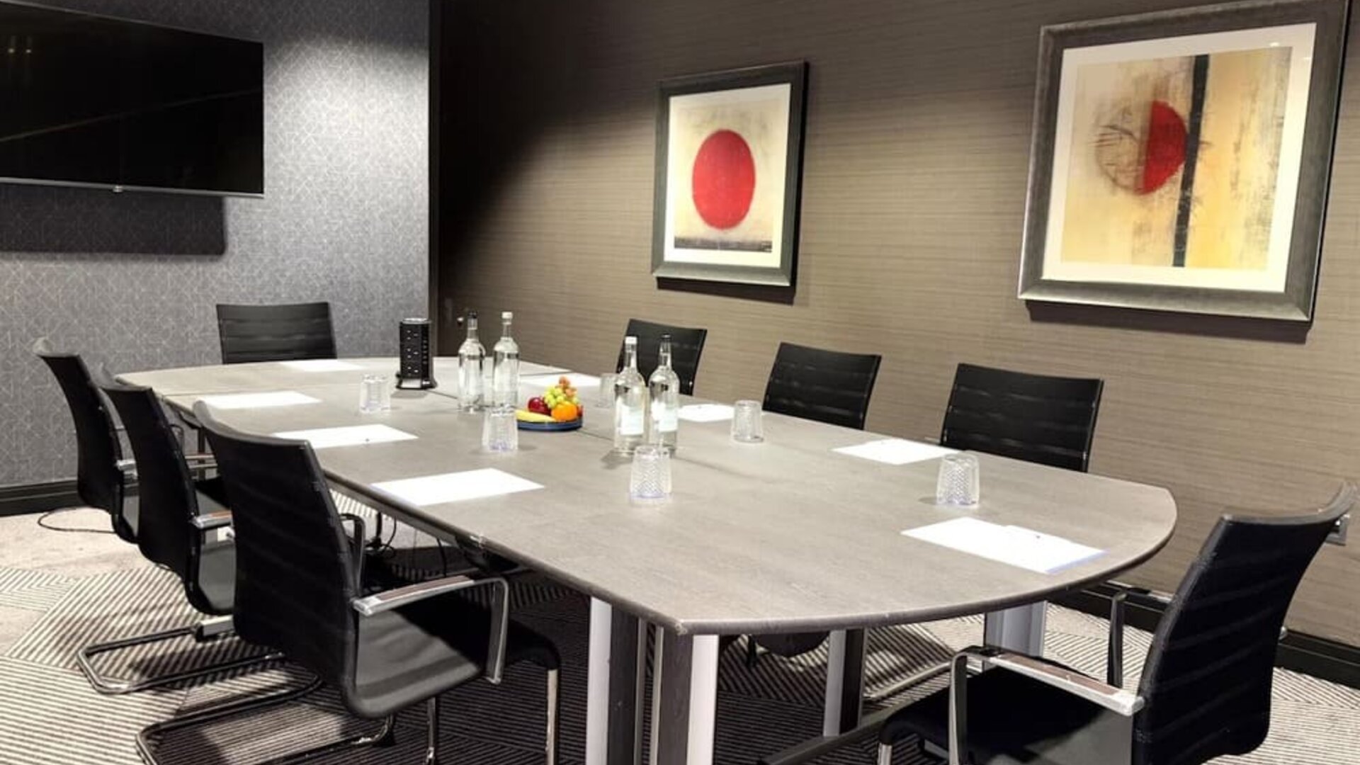 Meeting room with long conference table, black chairs, water bottles, and framed abstract artwork on walls