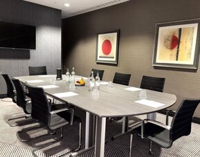 Meeting room with long conference table, black chairs, water bottles, and framed abstract artwork on walls