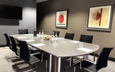 Meeting room with long conference table, black chairs, water bottles, and framed abstract artwork on walls