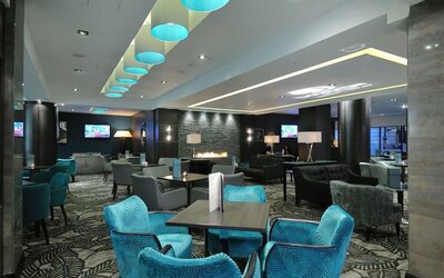 Modern lounge with teal chairs, patterned carpet, fireplace wall, and soft overhead lighting accents
